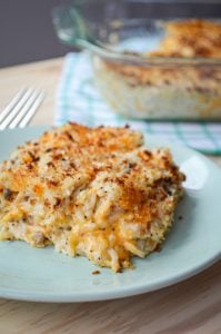 A portion of poppy seed chicken and rice casserole rests on a plate. A baking dish of casserole in the background.