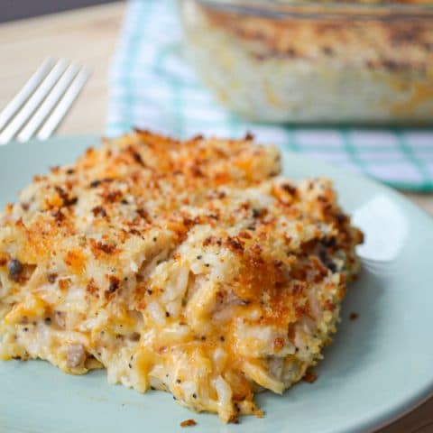 A portion of poppy seed chicken and rice casserole rests on a plate. A baking dish of casserole in the background.