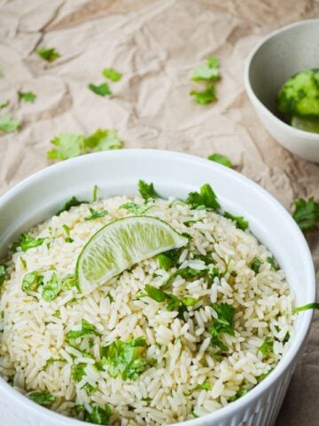 A dish full of cilantro lime rice on a brown paper covered table. Garnished with a lime wedge.