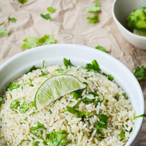 A dish full of cilantro lime rice on a brown paper covered table. Garnished with a lime wedge.