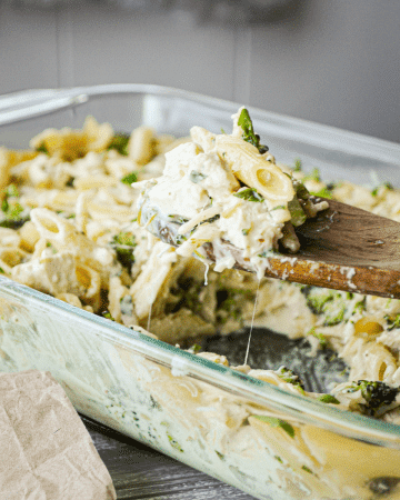 A baking dish of chicken broccoli alfredo casserole. A wooden spoon pulls out a portion.