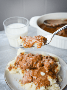 A plate of slow cooker pot roast and gravy served over mashed potatoes.