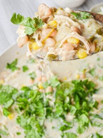 A bowl of chicken breast chili, with a spoon lifting out a portion.