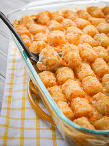 A serving spatula lifts a serving of Tater Tot and Ground Beef Casserole from a baking dish.