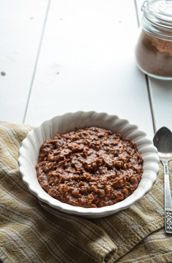 A bowl of chocolate peanut butter oatmeal resting on a cloth napkin, with some cocoa powder hanging out near by.