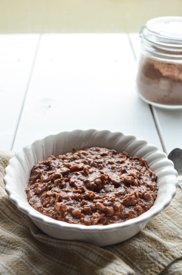 A bowl of chocolate peanut butter oatmeal resting on a cloth napkin, with some cocoa powder hanging out near by.