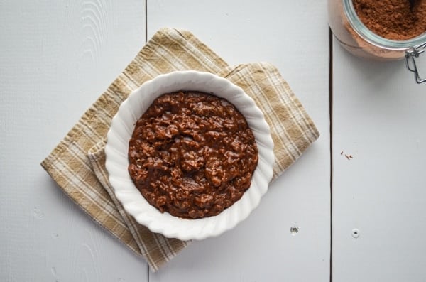 A bowl of chocolate peanut butter oatmeal resting on a cloth napkin, with some cocoa powder hanging out near by.