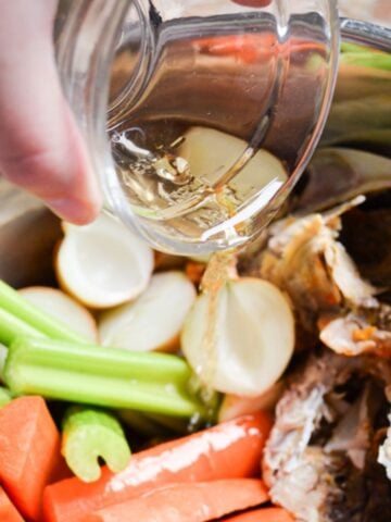 Pouring apple cider vinegar into an Instant Pot full of vegetables and meat bones.