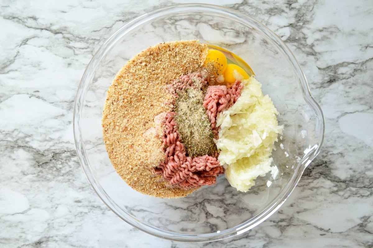 A bowl of the ingredients needed to make meatballs: lean ground beef, bread crumbs, eggs, seasonings, and onions.