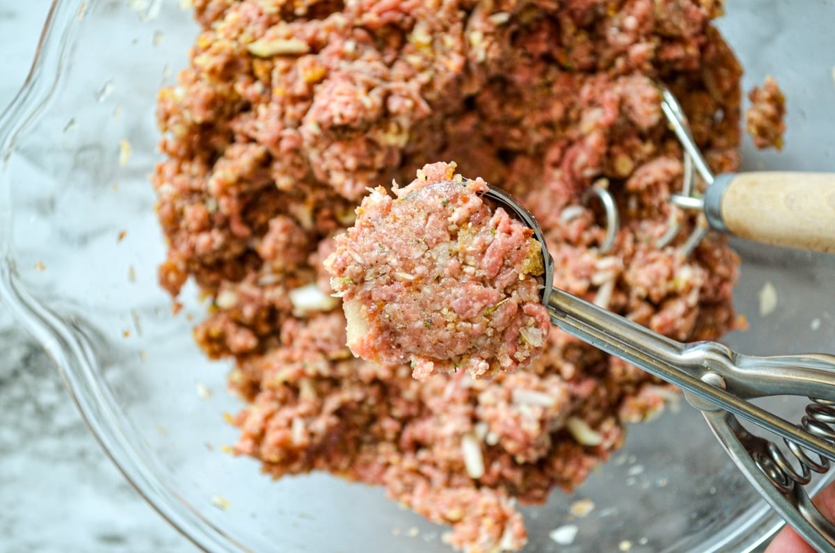 A scoop, pulling out a portion of ground beef mixture for freezer meatballs.