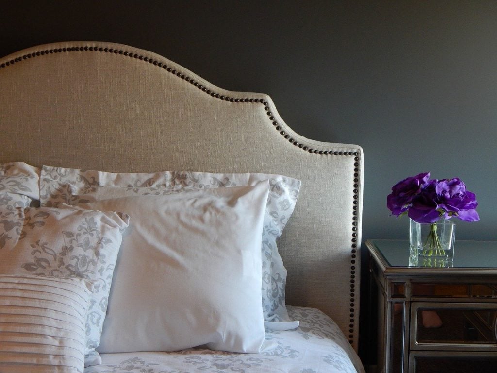 A bed with a fabric covered headboard. A nightstand to the right, with a small vase of flowers.