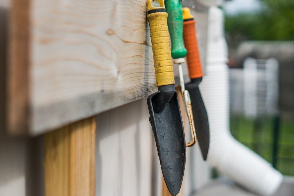 A garden hanging rack, holding two trowels and a fork.