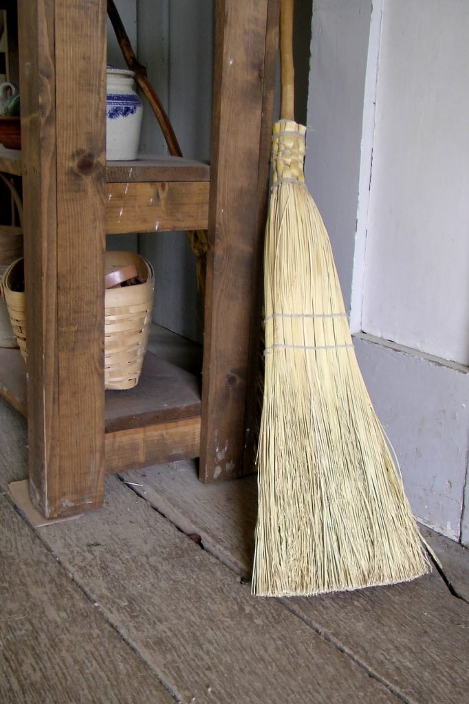 A corn broom resting against a shaker cabinet.