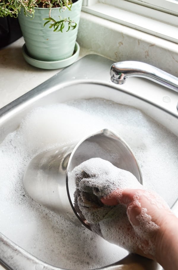 Washing dishes with a small potted rosemary plant to the left.