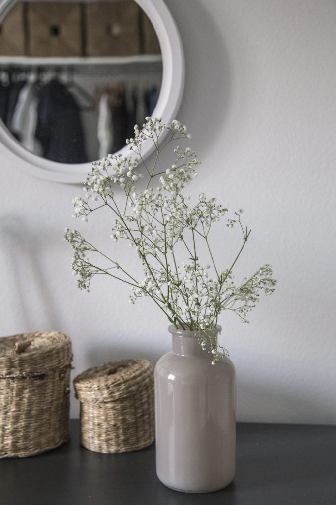 A vase of flowers on a dresser, with two small baskets. 