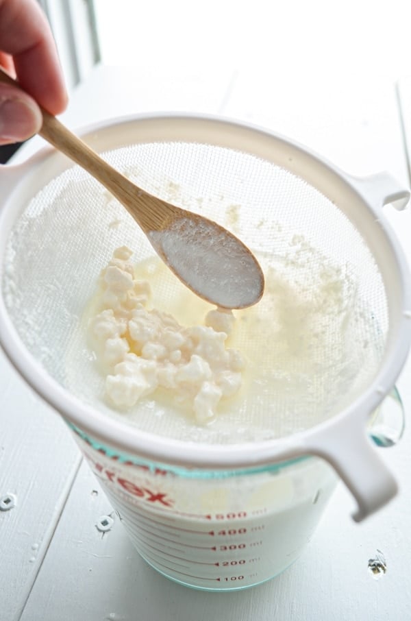 Use a wooden or plastic utensil to manipulate the grains and kefir, helping push the kefir through the strainer.
