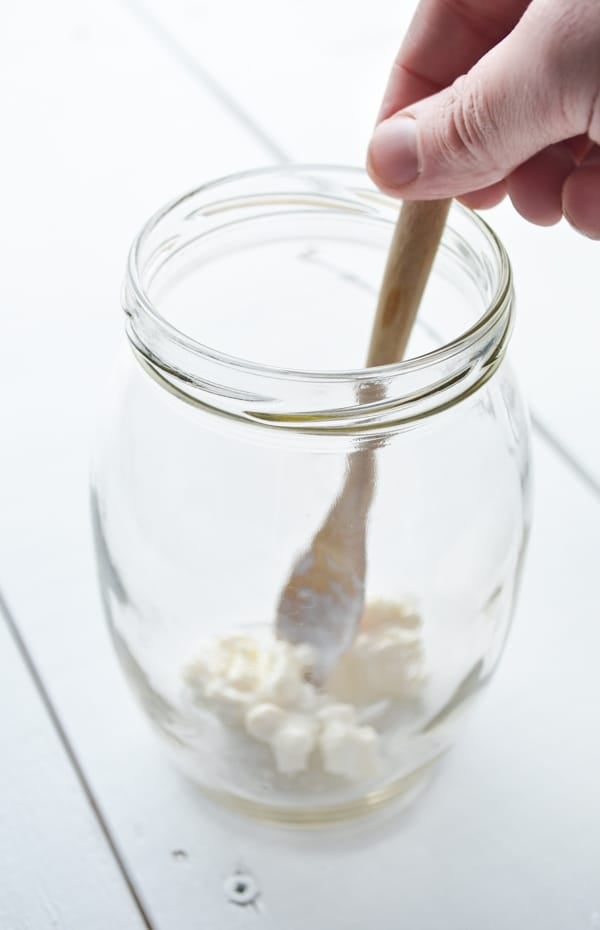 Adding the milk kefir grains to a clean glass jar is one of the first steps in making milk kefir. Here you see approximately 1 tbsp. of grains in a medium sized glass jar.
