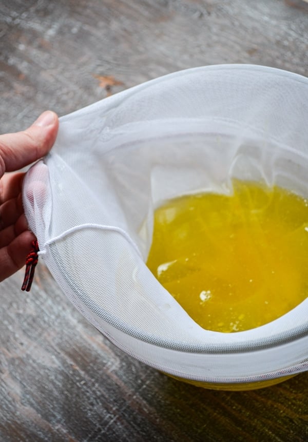 Removing the nut milk bag from the bowl, letting the homemade instant pot ghee to strain through, leaving the milk solids behind.