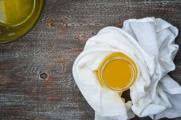 A jar of golden ghee in flatlay, surrounded by a white kitchen towel, and a bowl of freshly made Instant Pot Ghee.