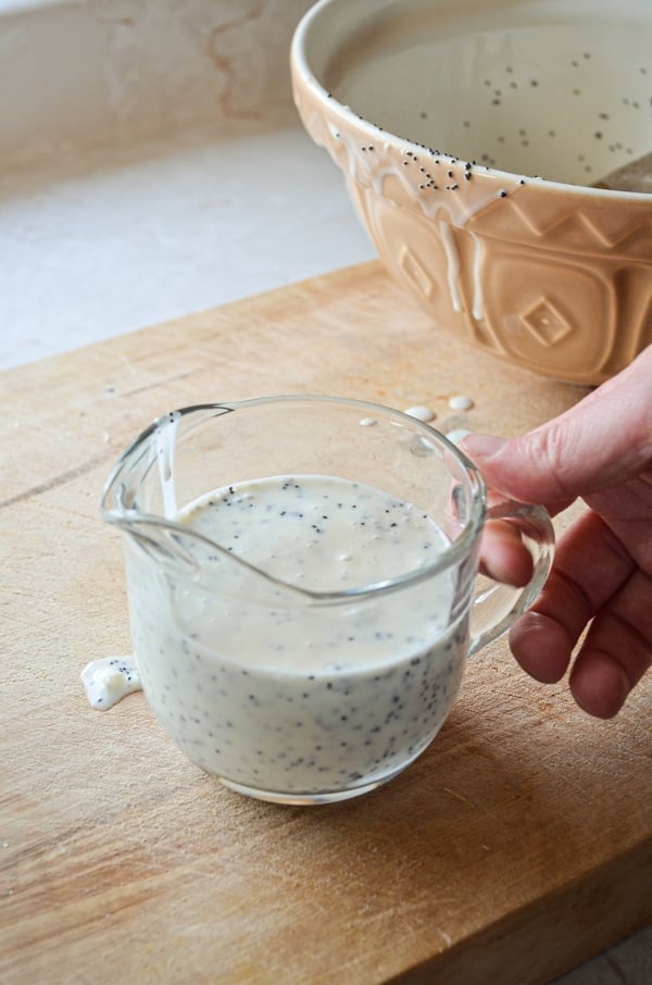 A small cruet of honey sweetened healthy poppy seed salad dressing, being held and ready to pour.