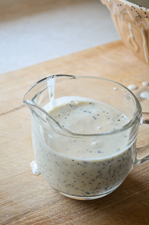 A small cruet of Honey Sweetened Healthy Poppy Seed Dressing sits on a cutting board.