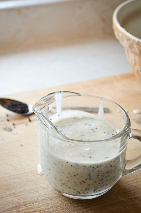 A small cruet of Honey Sweetened Healthy Poppy Seed Dressing sits on a cutting board.