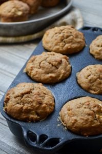 A cast iron muffin pan holding 6 delicious Apple Walnut Sourdough Discard Muffins.