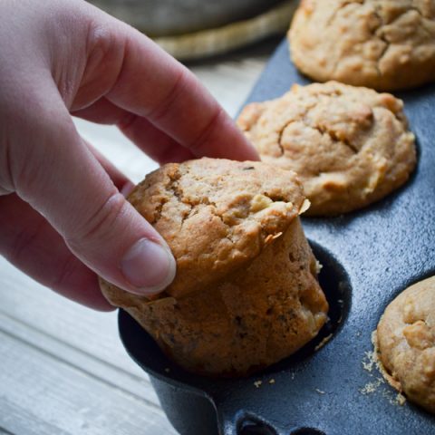 A hand pulls a sourdough muffin from a cast iron muffin pan.