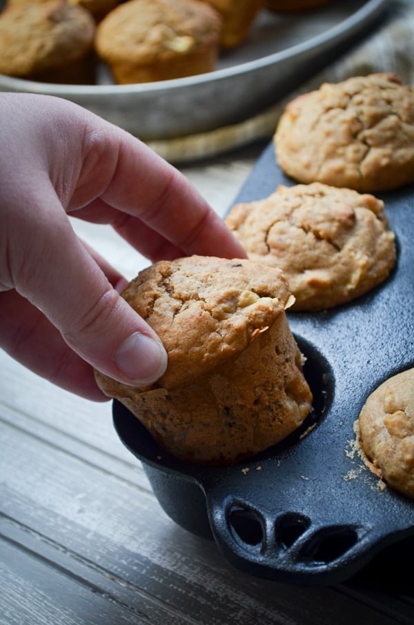 A hand pulls a sourdough muffin from a cast iron muffin pan.