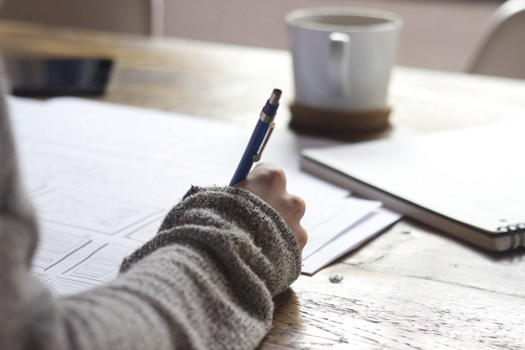 A woman writing a list , helping her to prepare for gardening season. A cup of coffee is in the background.