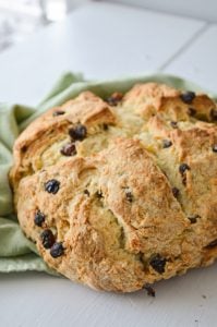 A loaf of sourdough discard Irish Soda bread, speckled with raisins and resting on a green cloth napkin.