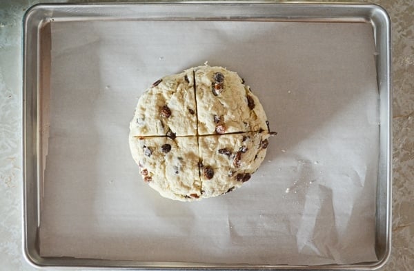 An unbaked loaf of Irish Soda Bread, scored and resting on a parchment lined baking sheet.