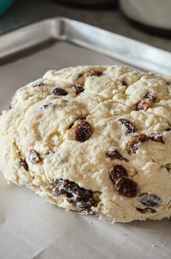 An unbaked loaf of Irish Soda Bread, scored and resting on a parchment lined baking sheet.