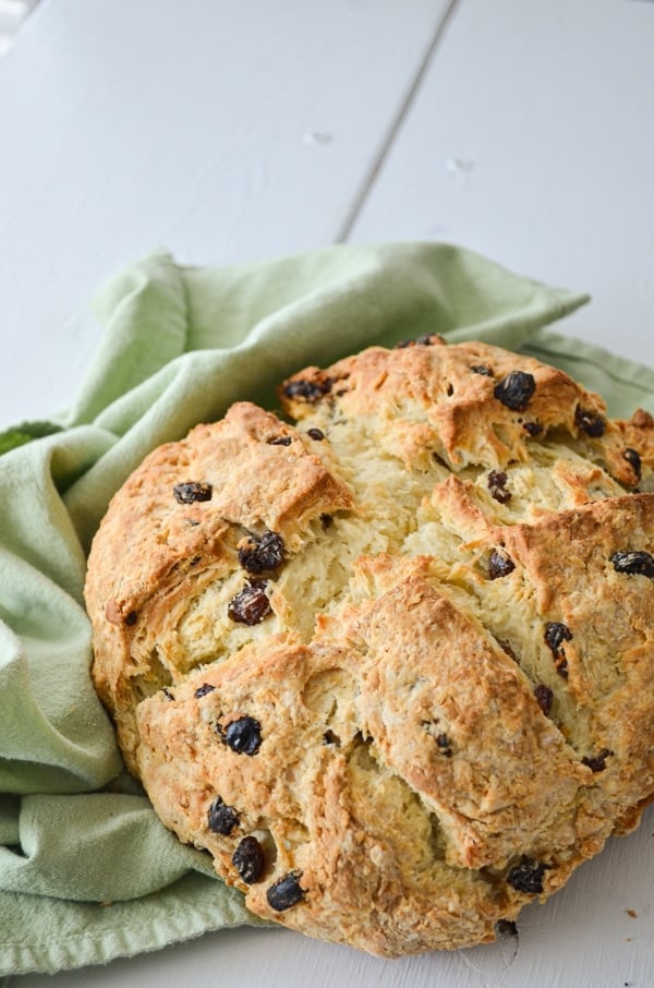 A loaf of sourdough discard Irish Soda bread, speckled with raisins and resting on a green cloth napkin.