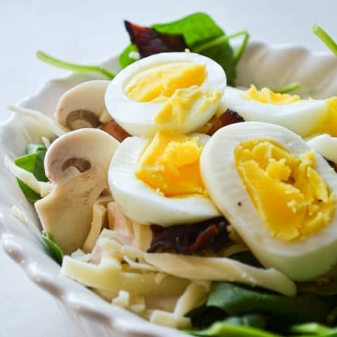 A small bowl of baby spinach salad, topped with hard-boiled eggs.