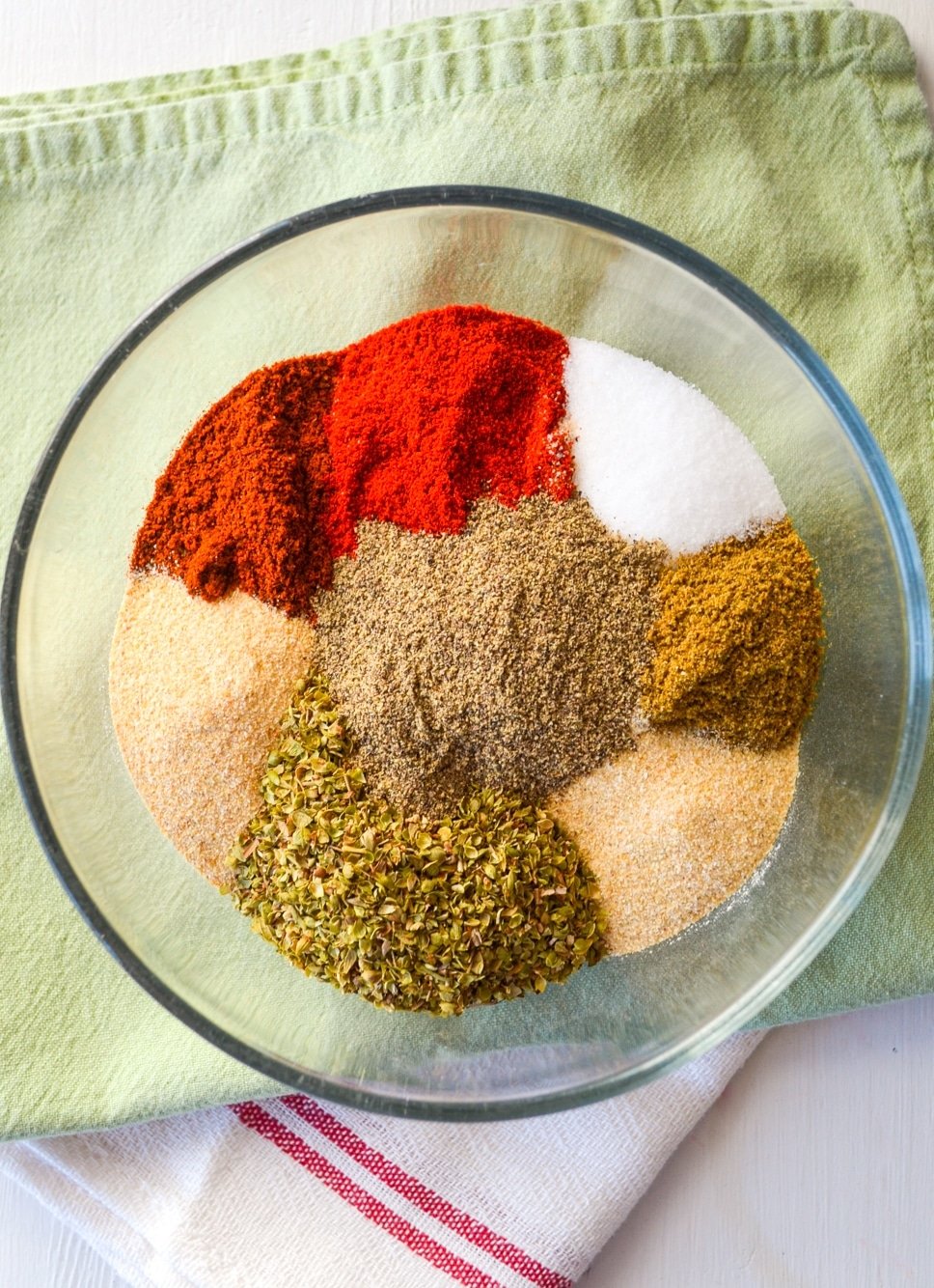 A glass bowl on top of green cloth napkin, with various seasonings within.