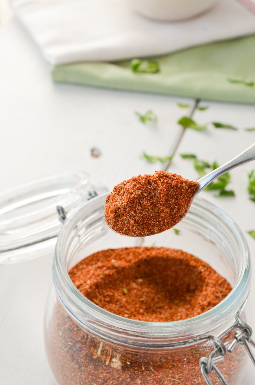 A jar of chicken taco seasoning, with a small spoon taking some out. Cilantro sprinkled in the background.