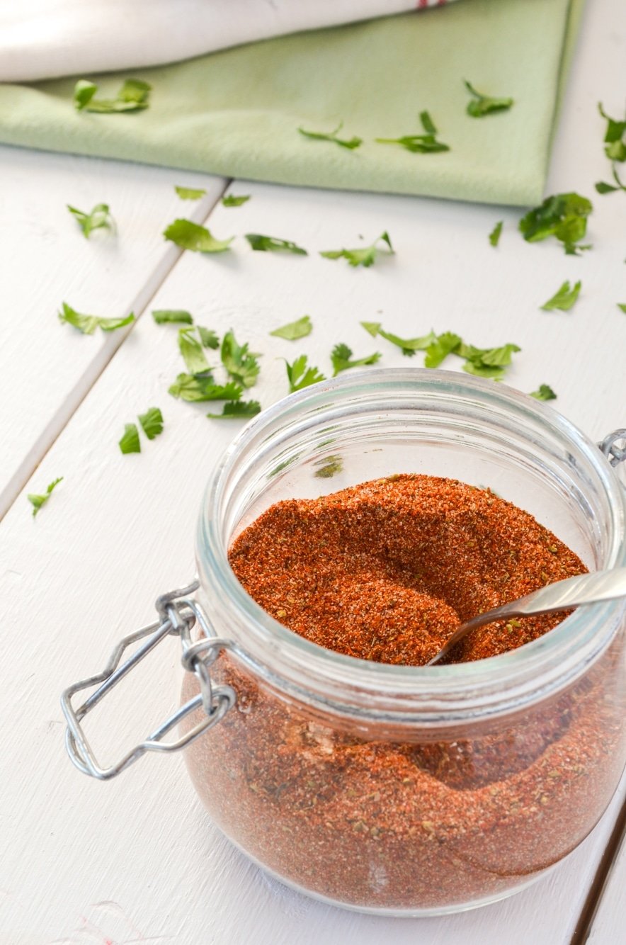 A jar of taco seasoning on a white table, cilantro scattered all over the top.