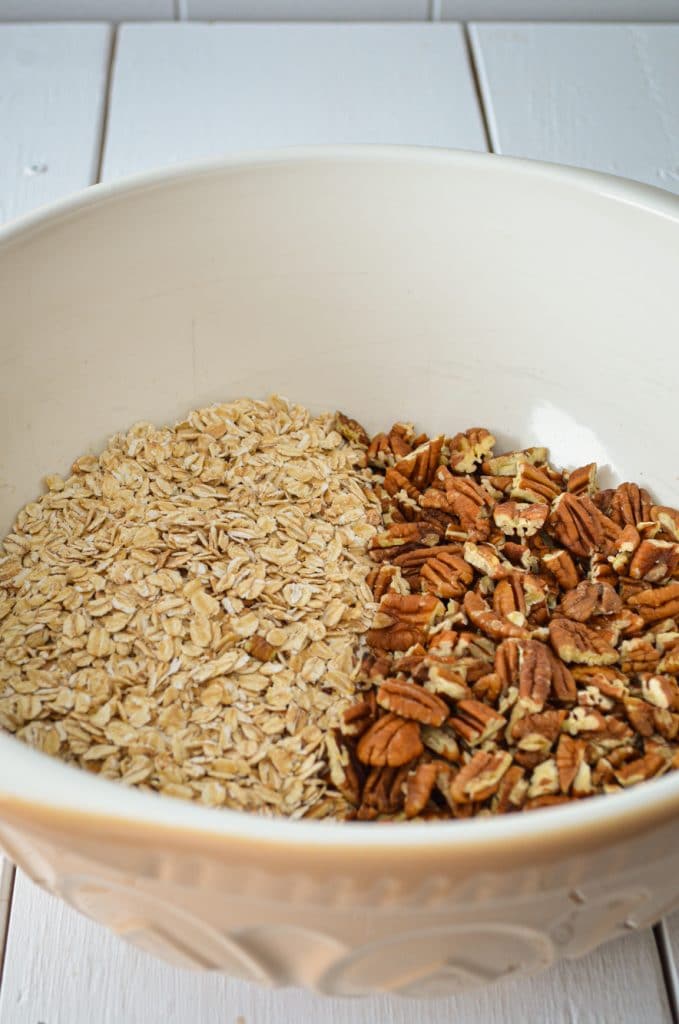 A large mixing bowl, containing dry oats and pecans.