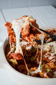 A baking dish of cheesy tortellini bake, with a portion being pulled out. Big strings of cheese connect the serving to the casserole.