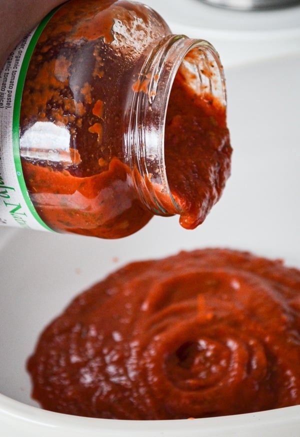 A jar of pasta sauce being poured into a baking dish.