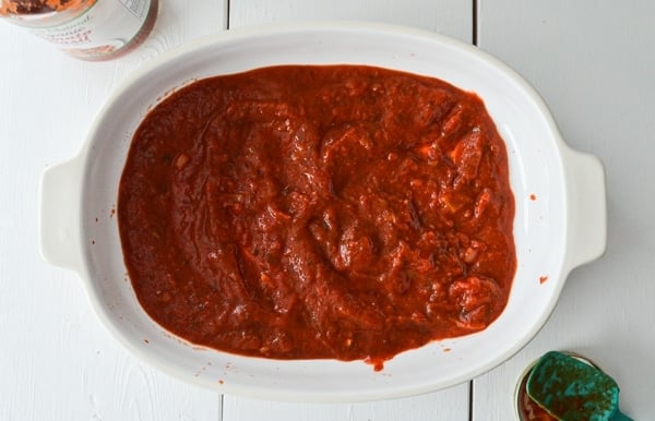 Pasta sauce is spread into the bottom of a baking dish.