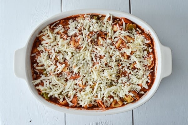 A baking dish is filled with tortellini and pasta sauce. Topped with shredded mozzarella cheese.
