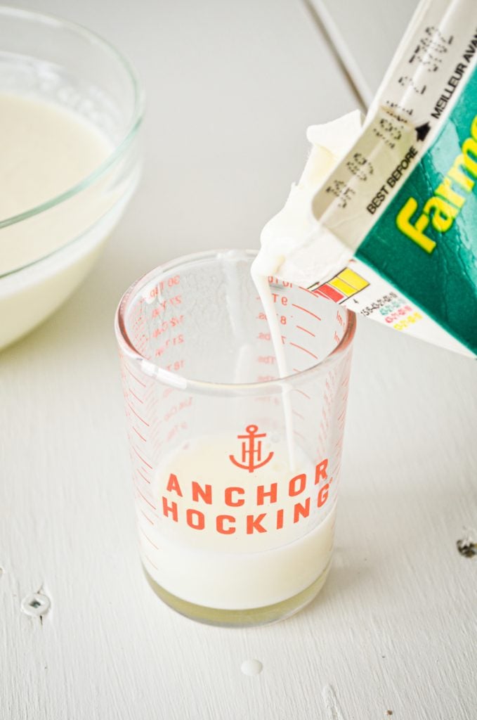 Buttermilk being poured into a small measuring cup.