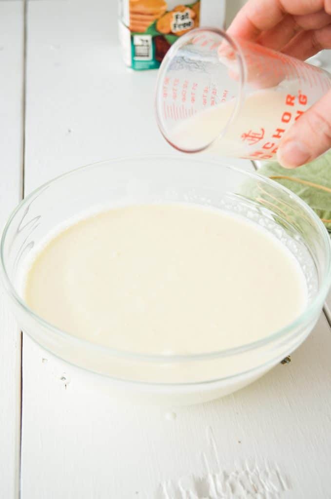 A measuring cup pours buttermilk into a bowl of heavy cream.