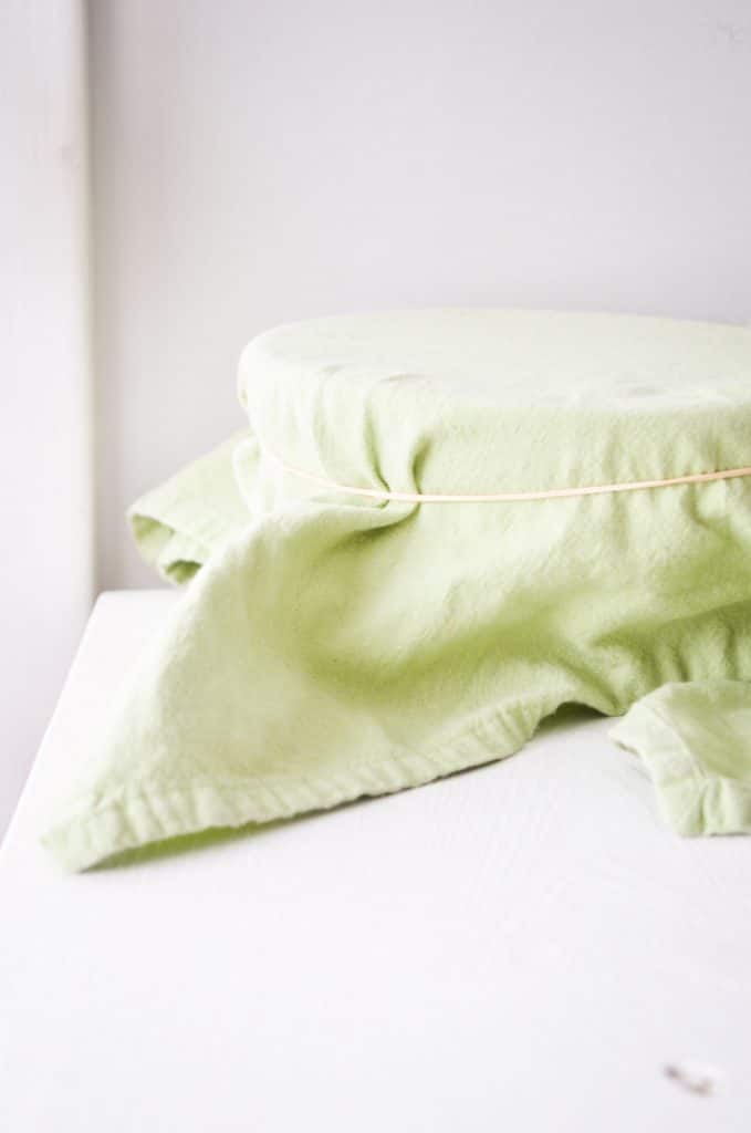 A bowl rests on the back of a table with a tea towel on top, secured by a rubber band.