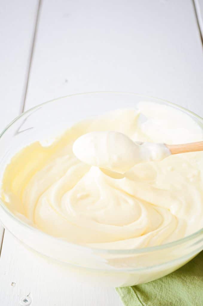 A bowl of creme fraiche, a wooden spoon lifting up a portion.