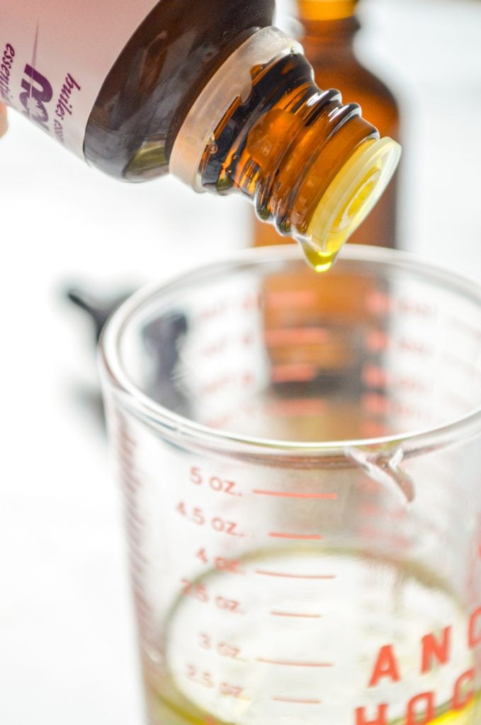 A bottle of orange essential oil, dropping into a small measuring cup.