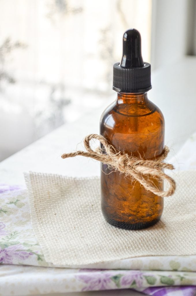 A bottle of facial serum with a piece of twine wrapped around the bottle, resting on several layers of fabric.