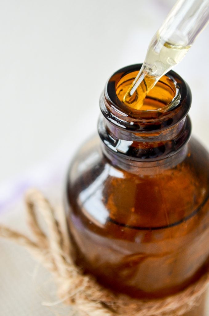 A close up of a amber jar with the dropper being removed; drops of facial serum dripping out.